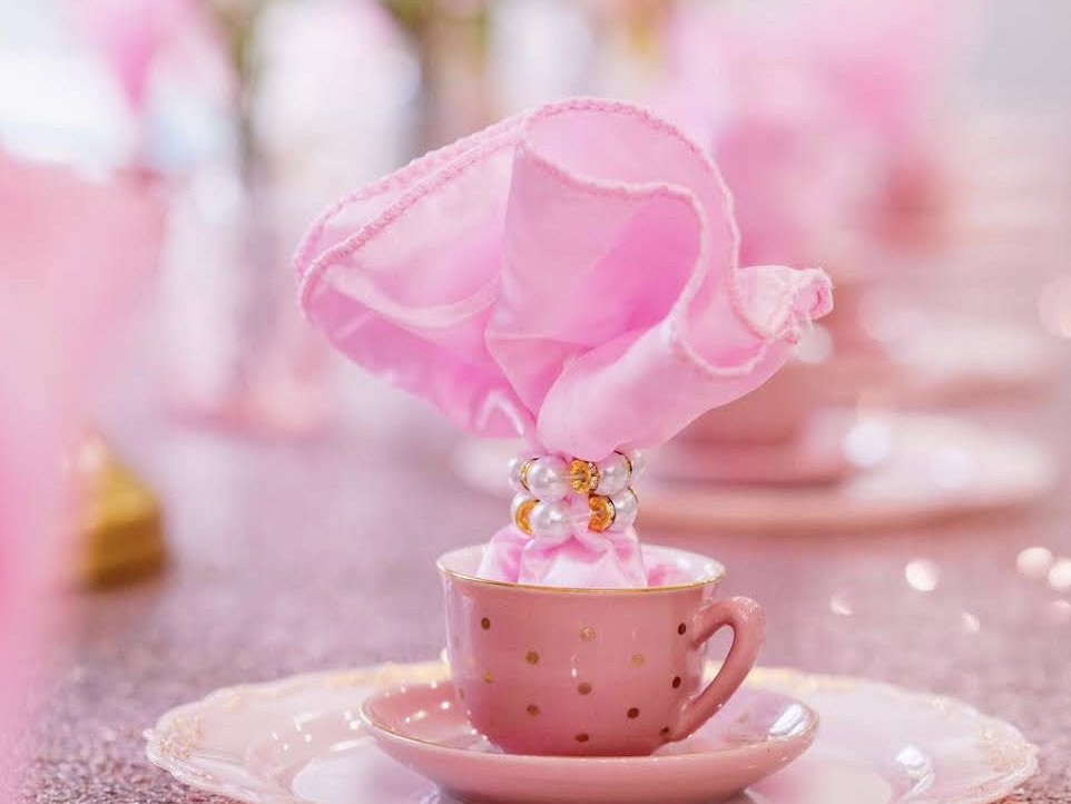 A pink teacup with a ruffled napkin in a pearl ring on a glittering table at the Princess Character Breakfast