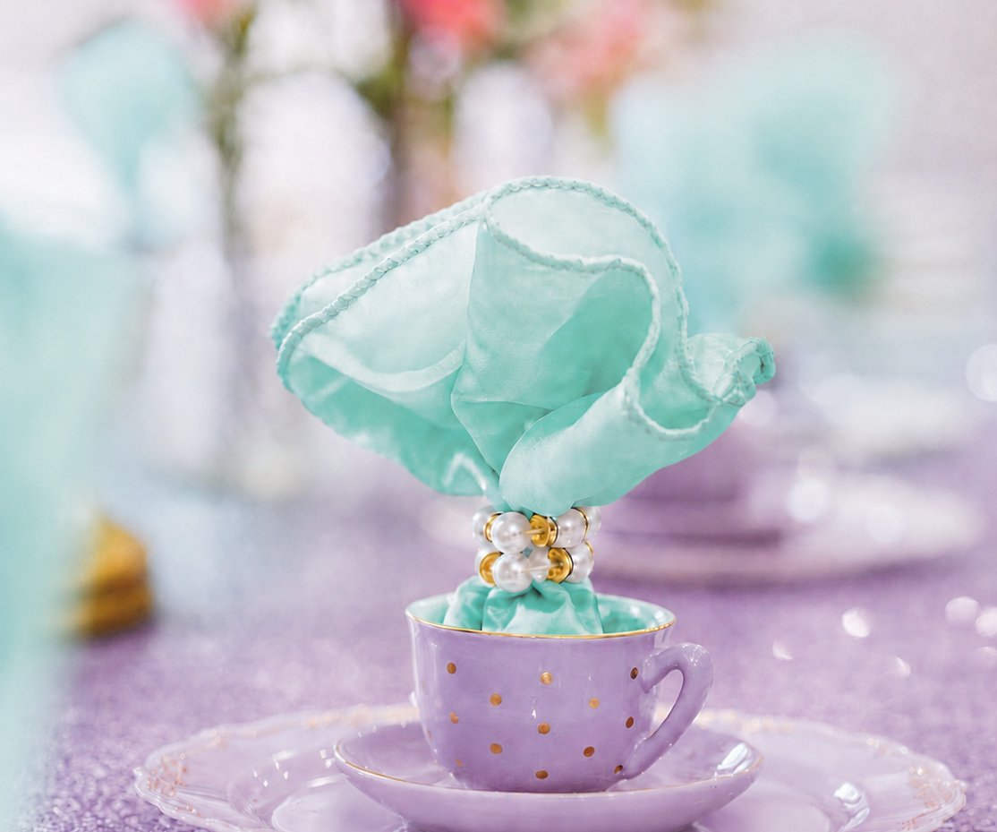 A lilac teacup with a gold spot and a mint napkin in a pearl ring at the Mermaid Character Breakfast