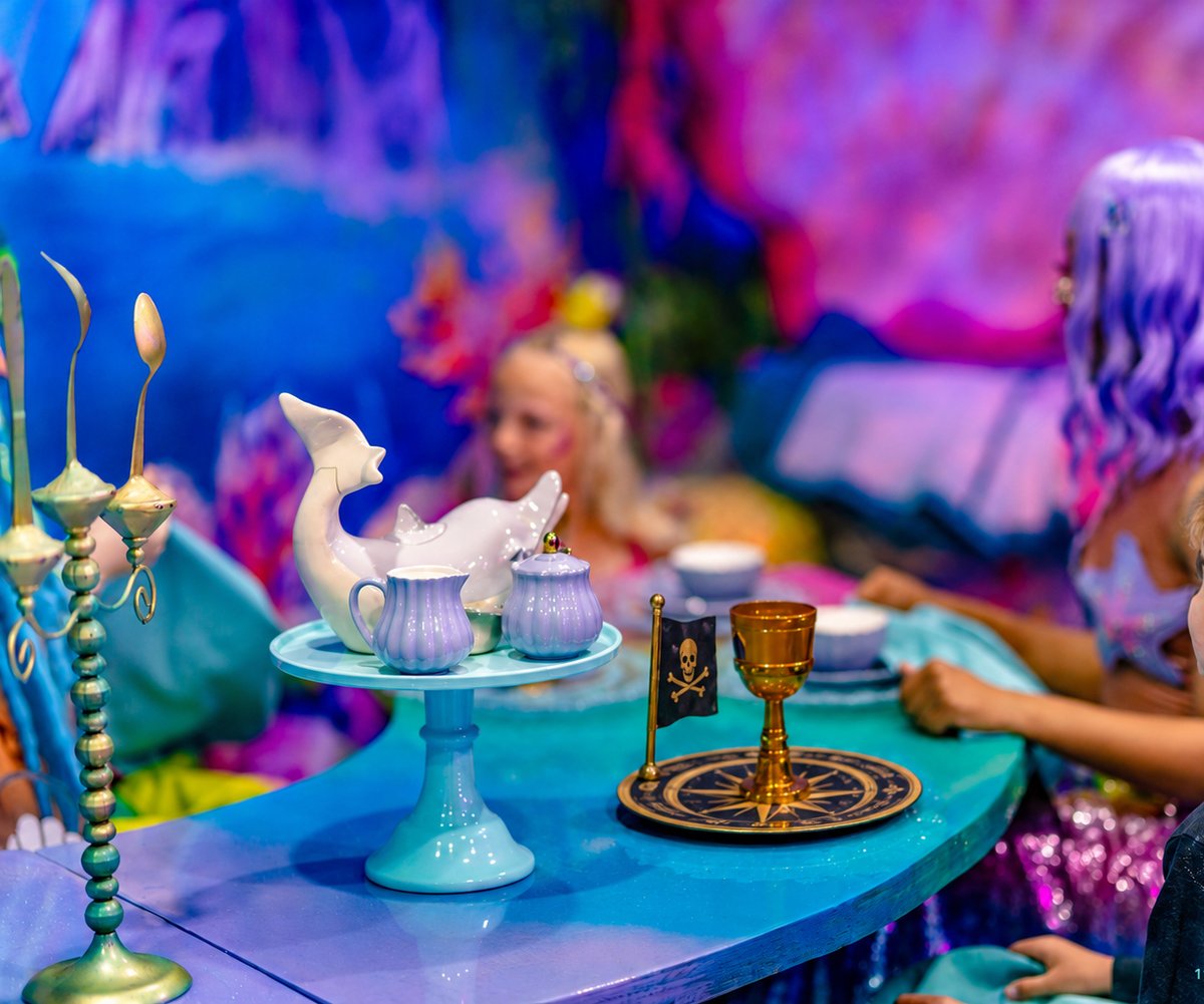 A purple and teal mermaid tea table with a skull flag and a gold goblet at a Mermaid and Pirate Party