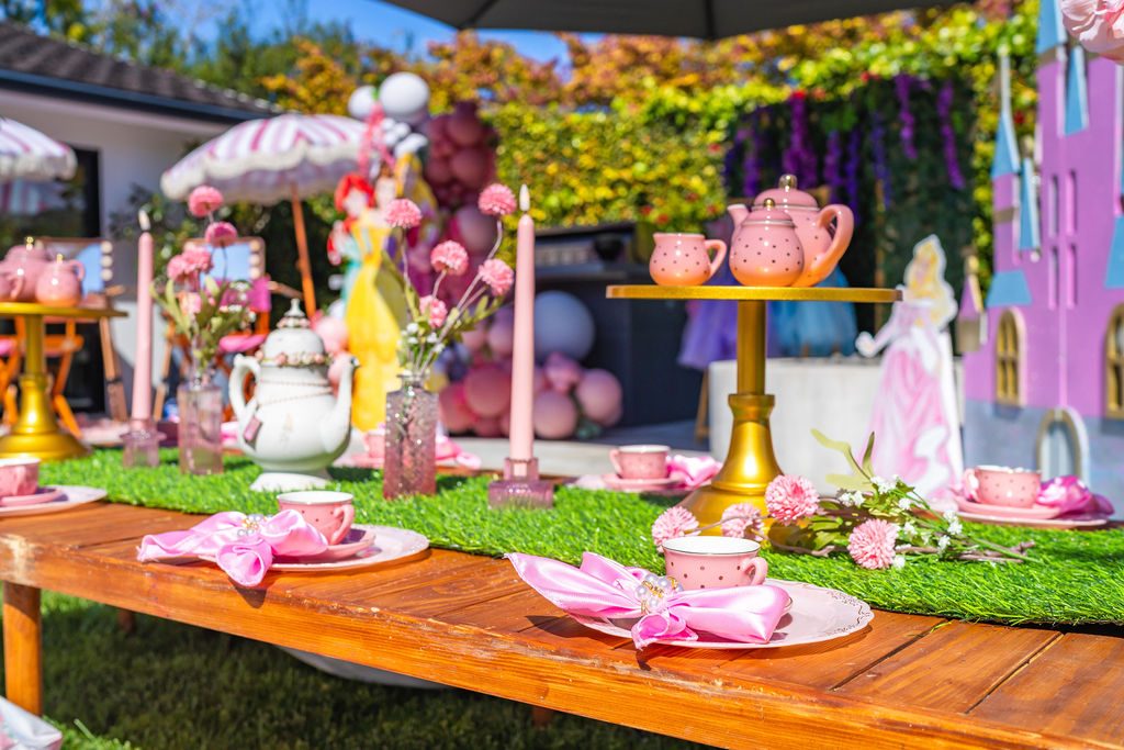 A decorated picnic table set with shell plates, cloth napkins, teapots and flowers