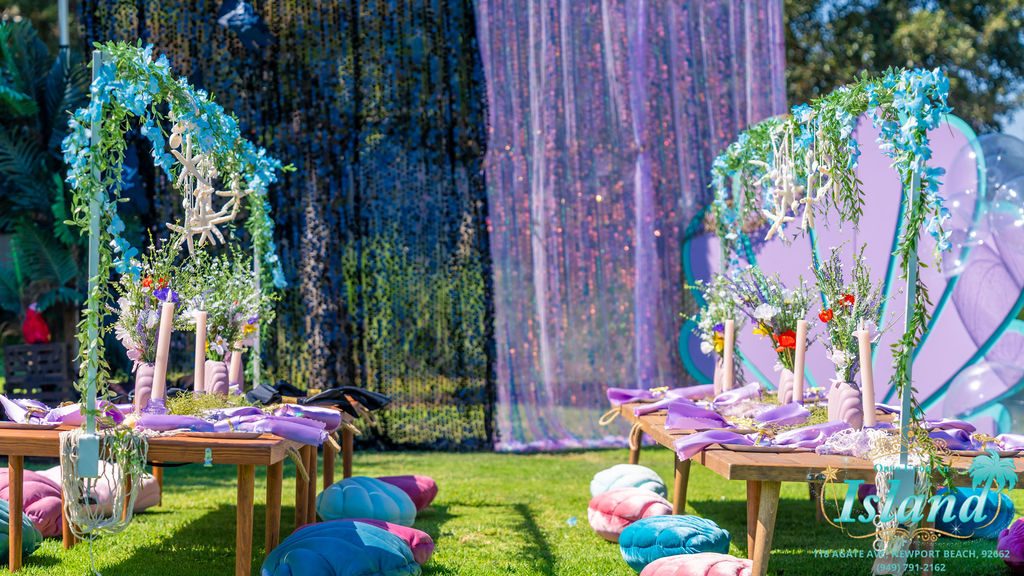 A mermaid party built in a park, with the shell arch and the decorated tables