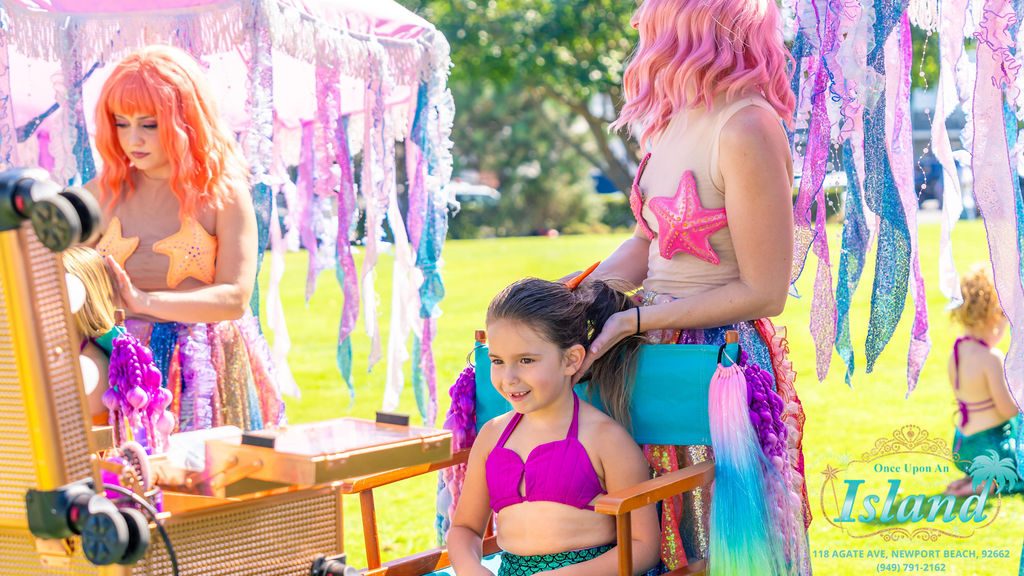 A stylist braiding a child’s hair in the salon chair at a traveling makeover station