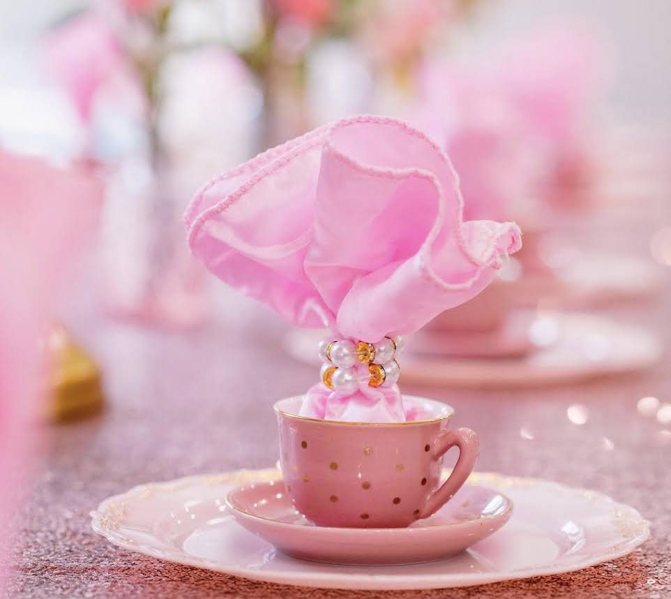 A pink place setting with a gold-spotted teacup and a ruffled napkin at an Ultimate Princess Tea Party