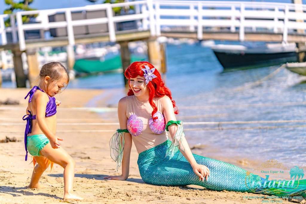 The Mermaid Princess and a child playing on the beach beside the harbour