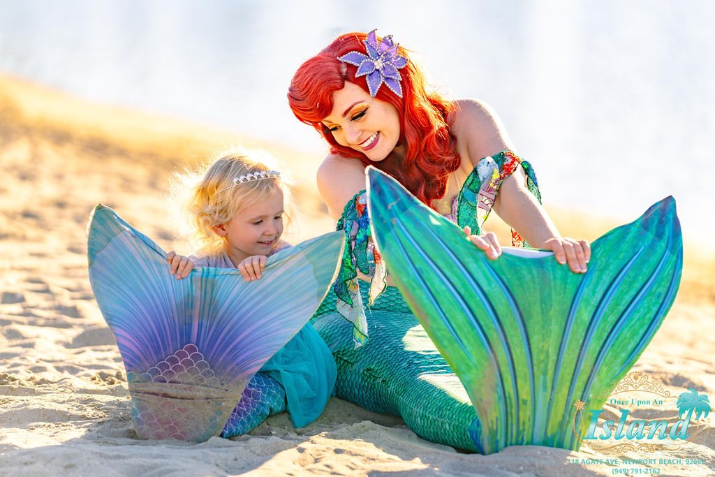 The Mermaid Princess in her tail on the sand with a young guest