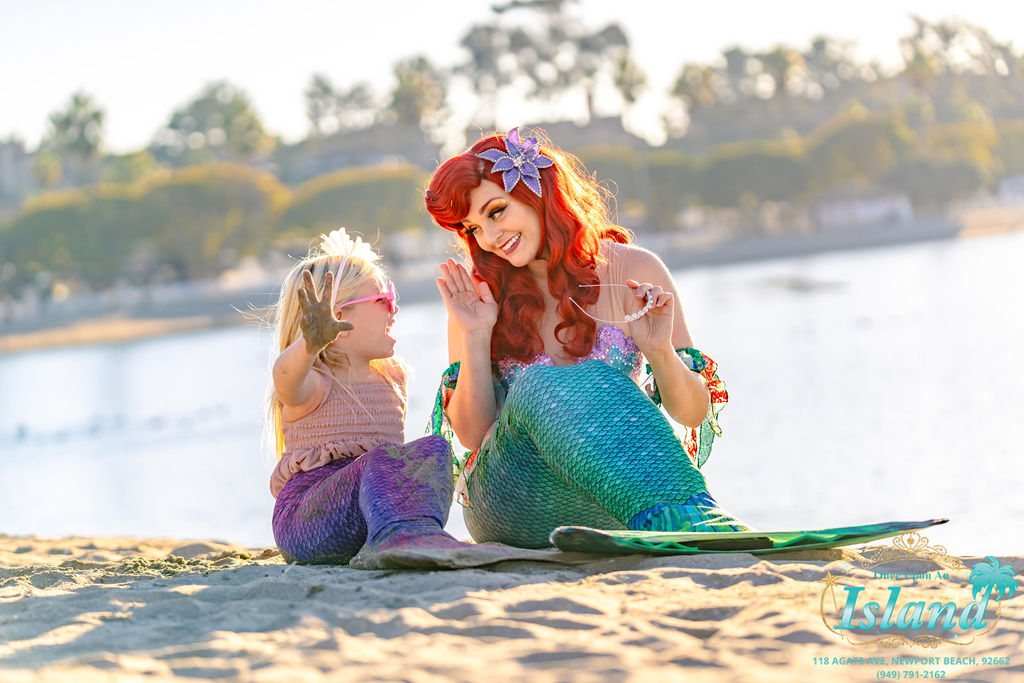 The Mermaid Princess and a child sitting together on the sand by the bay