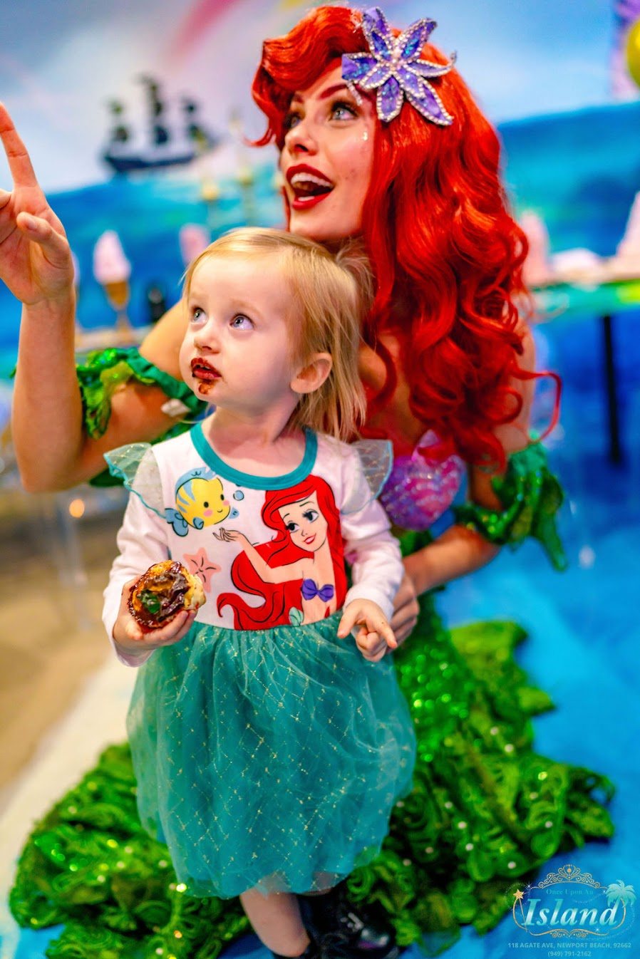 A birthday girl beaming beside the Mermaid Princess in front of a pirate ship backdrop