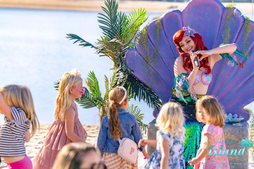 The Mermaid Princess in the clamshell with a circle of children listening