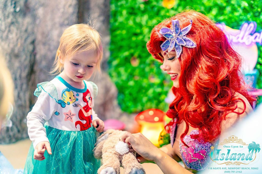 The Mermaid Princess handing a toddler a gift at a garden birthday