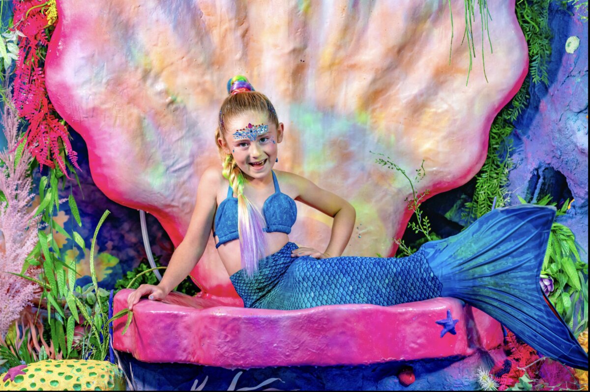 A child transformed into a mermaid on the clamshell throne during the VIP Mermaid Transformation